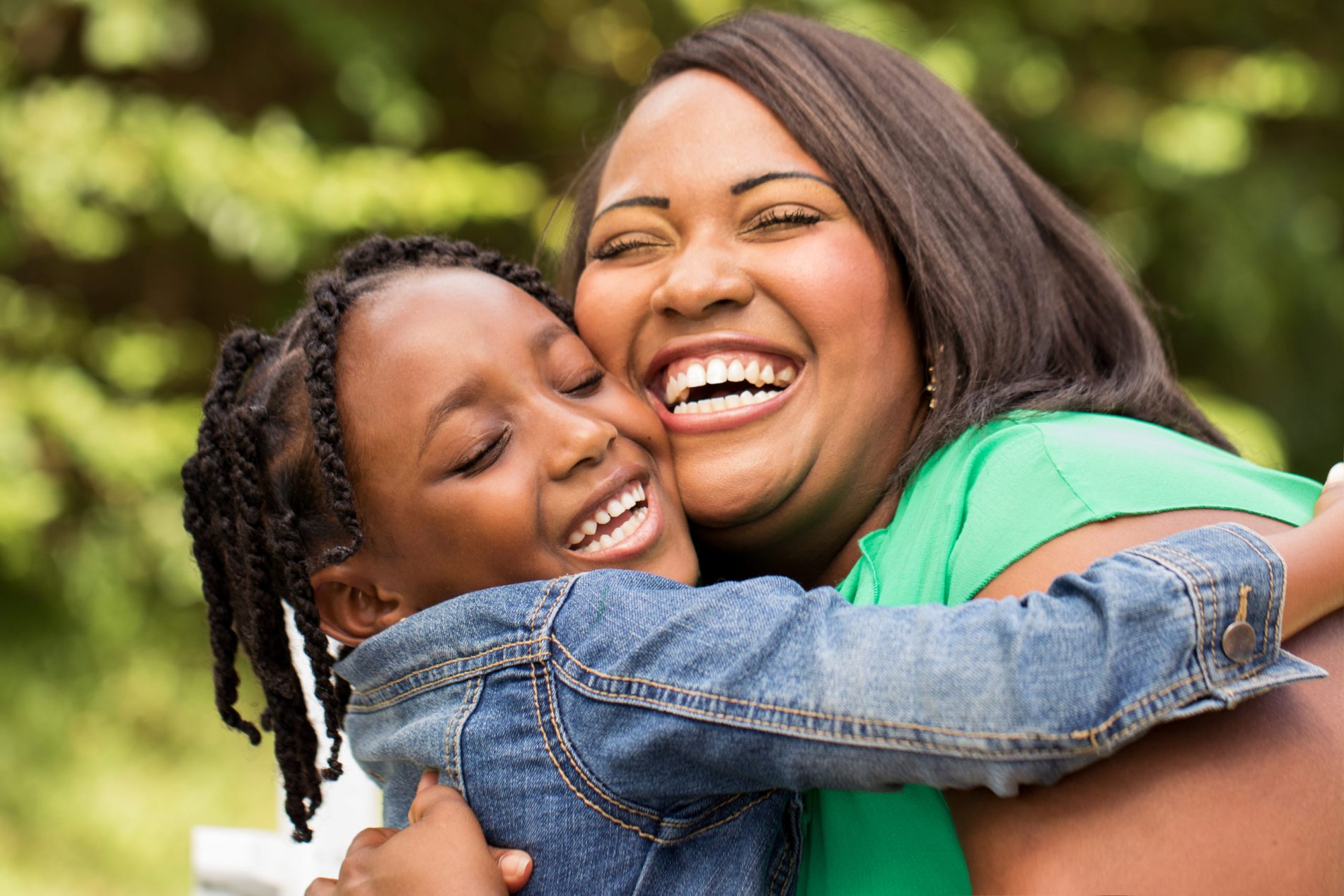 A happy Black mother and her daughter hugging and smiling outdoors