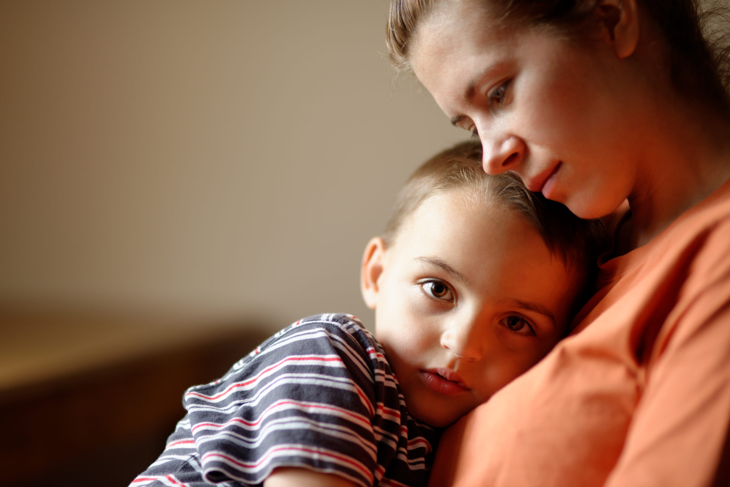 A woman with an orange shirt sitting with her young son cuddled onto her chest